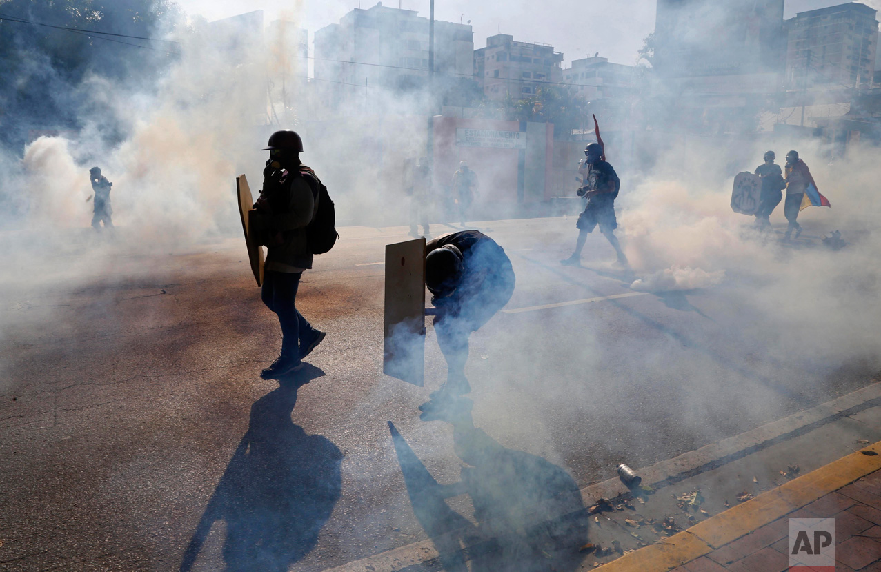 Anti-government protesters shield themselves from tear gas canisters as security forces disperse an opposition march and block them from reaching the Interior Ministry in Caracas, Venezuela, on Thursday, May 18, 2017. Venezuela has reached almost two months of anti-government unrest in which more than 40 people have been killed. (AP Photo/Ariana Cubillos)