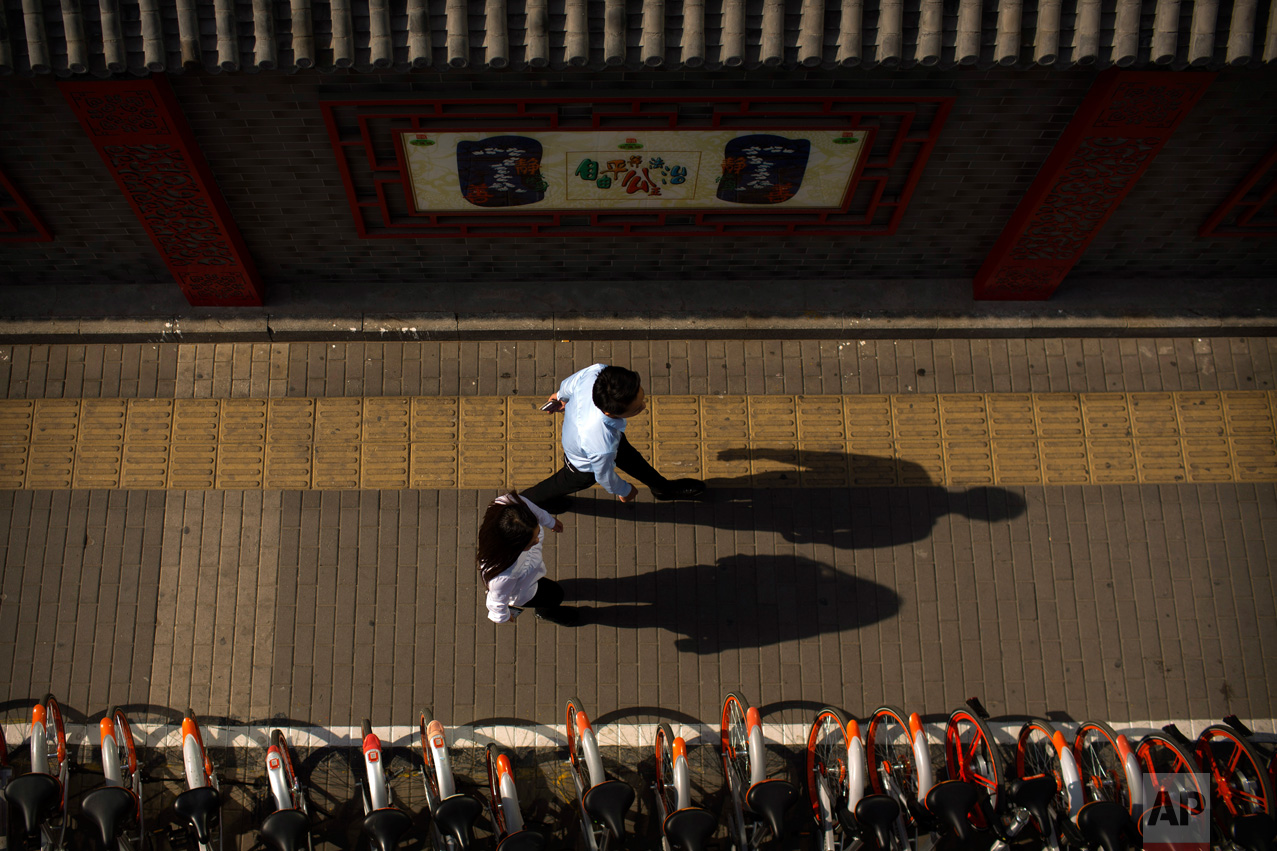 Pedestrians cast shadows as they walk along a sidewalk in Beijing, Thursday, May 25, 2017. (AP Photo/Mark Schiefelbein)