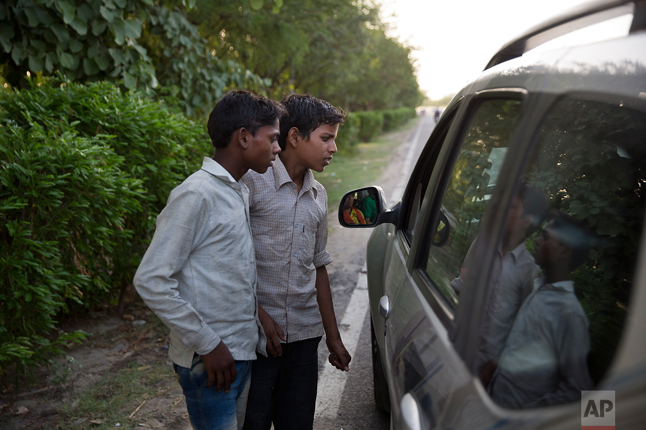  In this Thursday June 8, 2017 photo, Indian boys Salish 15, left, and Sachin 12, listen to their customer as they sell cooked corn along a busy expressway in Noida, India. Every 100 meters (330 feet) or so there are children selling corn along this 