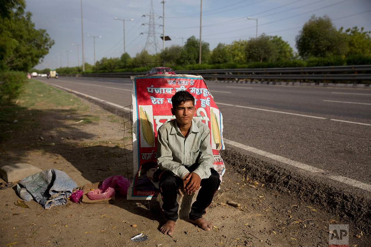  In this Thursday June 8, 2017 photo, Indian boy Bhure, poses as he sits near his make shift corn stall along a busy expressway in Noida, India. Bhure says he at times receives job offers from some of his customers promising double of what he earns. 