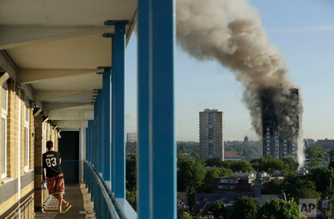  A resident in a nearby building watches smoke rise from a building on fire in London, Wednesday, June 14, 2017. Grief turned to outrage Friday amid reports that materials used in the building's renovation could have fueled the inferno that left doze