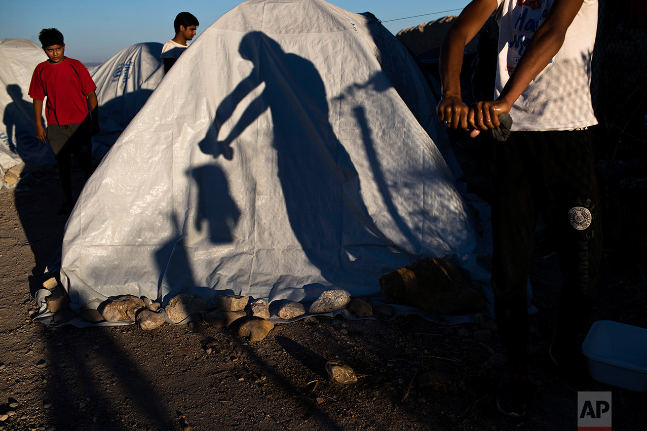  In this June 9, 2017 photo, a Pakistani migrant wrings a t-shirt as his shadow falls on a tent at a beach near the Souda refugee camp, where hundreds refugees and other migrants live in makeshift tents on Chios island, Greece. (AP Photo/Petros Giann