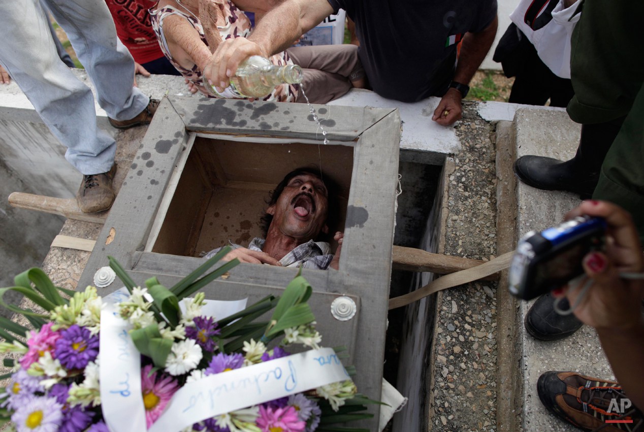  In this Feb. 5, 2014 photo, Divaldo Aguiar, who plays the part of Pachencho, lies inside a mock coffin as villagers splash rum into Aguiar's mouth during the Burial of Pachencho celebration at a cemetery in Santiago de Las Vegas, Cuba. The bash kick