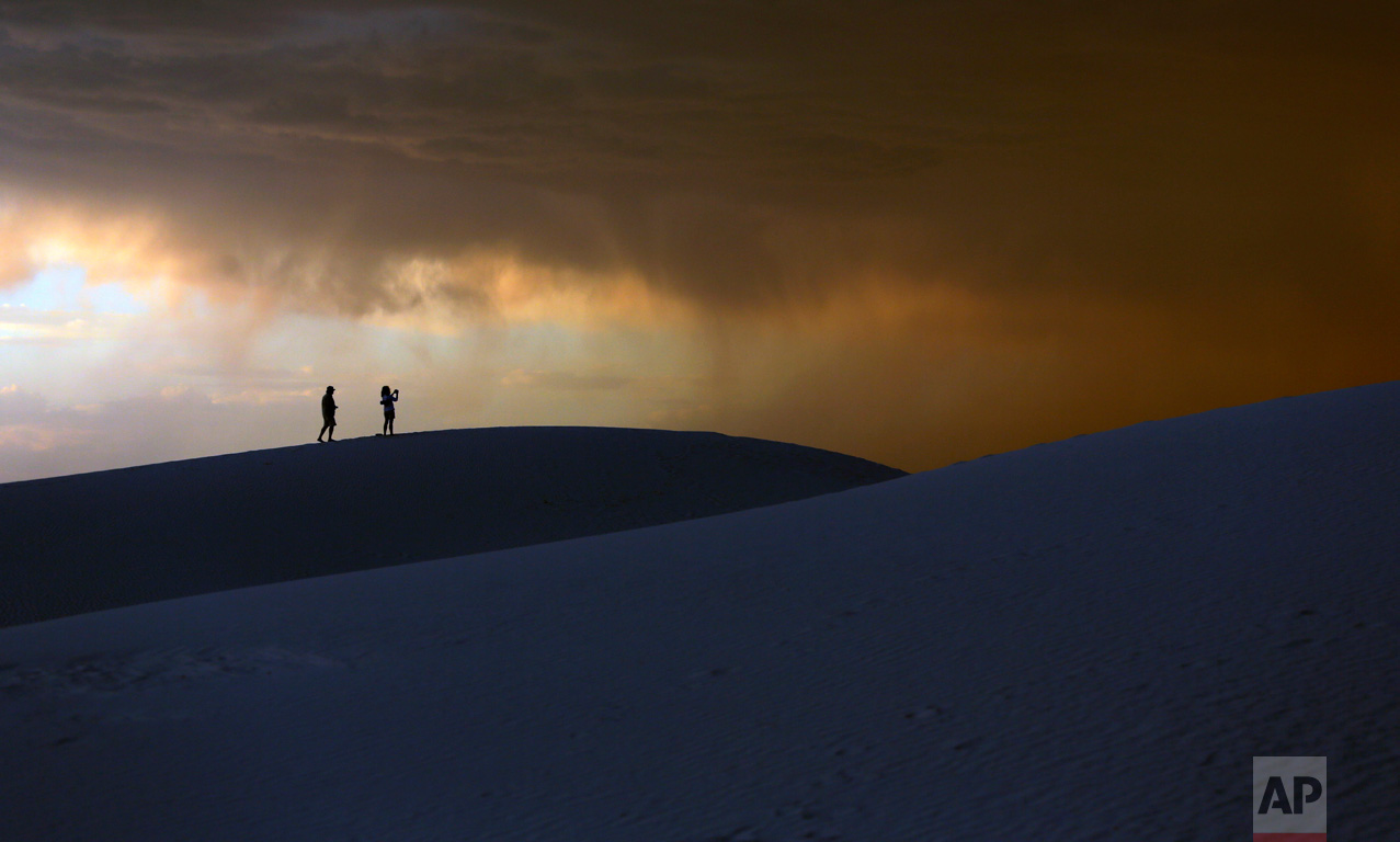 A storm moves in over a couple visiting White Sands National Monument, Wednesday, June 21, 2017, near Alamogordo, N.M. Temperatures in the area hit 105 degrees Wednesday. (AP Photo/Eric Gay)