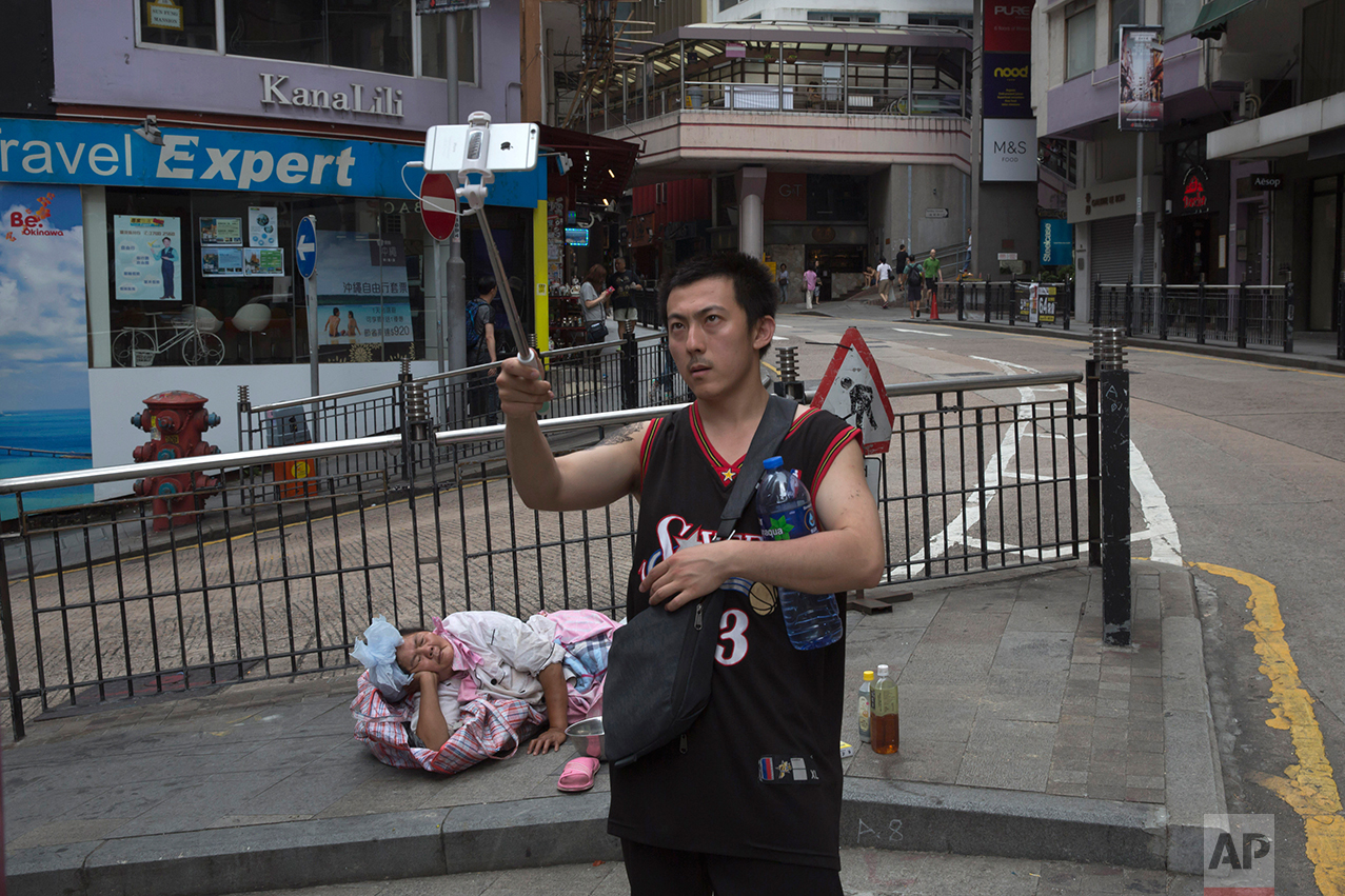 In this June 4, 2017, photo, a man takes a selfie with a homeless woman in Central district, Hong Kong. (AP Photo/Kin Cheung)