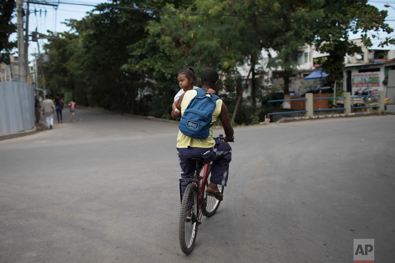 In this June 12, 2017 photo, Almir Arruda carries his daughter Jamile on his bike away from a morning shootout between police and drug traffickers in the City of God slum in Rio de Janeiro, Brazil. (AP Photo/Leo Correa)
