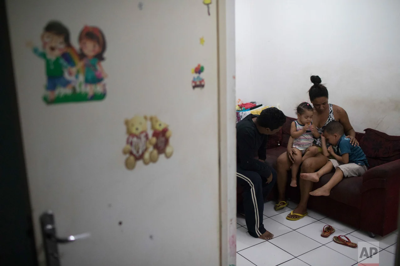 In this June 9, 2017 photo, Thaisa da Silva Ribeiro calms her four-year-old son Isaac, right, and two-year-old daughter Isadora as her husband Silvio Cesar Soares Gonzaga sits with them after a military police tank drove through their neighborhood in the City of God slum of Rio de Janeiro, Brazil. (AP Photo/Leo Correa)