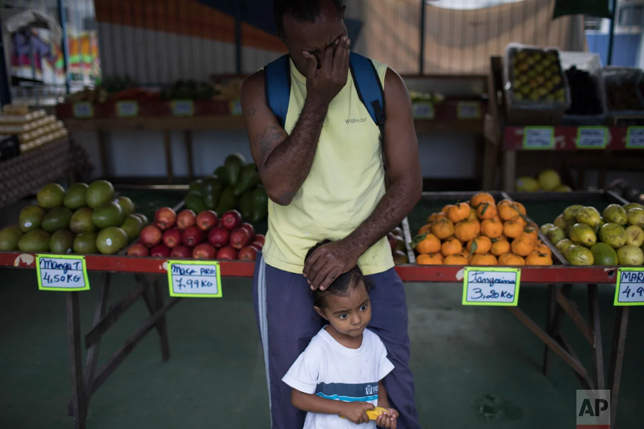 In this June 12, 2017 photo, Almir Arruda wipes tears as he waits for a shootout between drug traffickers and police to stop, as he stands over his four-year-old daughter Jamile in the City of God slum of Rio de Janeiro, Brazil. (AP Photo/Leo Correa)