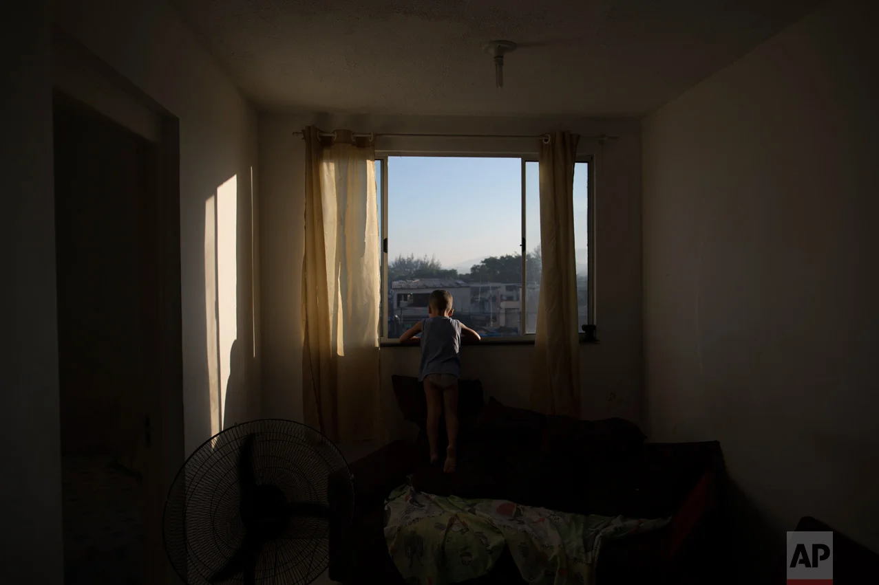 In this June 8, 2017 photo, four-year-old Isaac peeks out his apartment window in the City of God slum of Rio de Janeiro, Brazil, after his mother pulled him inside when a military police suddenly appeared in the street. (AP Photo/Leo Correa)