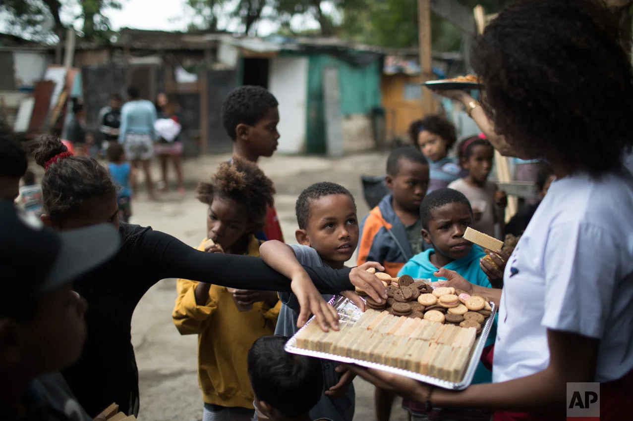 In this June 10, 2017 photo, kids help themselves to snacks being handed out by an NGO in one of the poorest area of the City of God slum in Rio de Janeiro, Brazil. (AP Photo/Leo Correa)