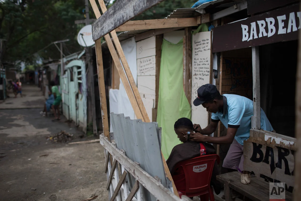 In this June 10, 2017 photo, a barber cuts a client's hair at his shop in the "Cantinho do Ceu" neighborhood that means in Portuguese "Heaven's corner," one of the poorest areas of the City of God slum in Rio de Janeiro, Brazil. (AP Photo/Leo Correa)