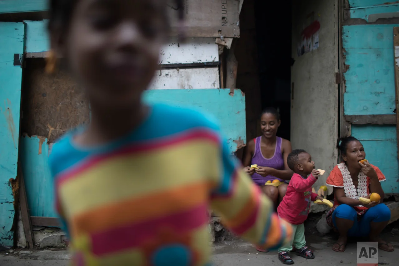 In this June 10, 2017 photo, women and children eat fruit distributed by an NGO in one of the poorest areas of the City of God slum in Rio de Janeiro, Brazil. (AP Photo/Leo Correa)