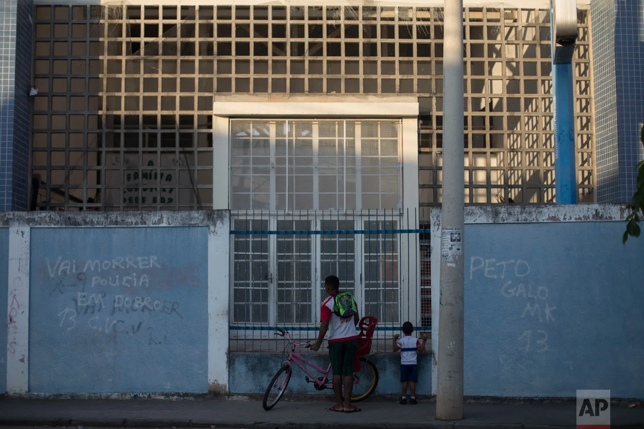 In this June 7, 2017 photo, a father waits for his son's gated school to open in the morning in the City of God slum of Rio de Janeiro, Brazil. (AP Photo/Leo Correa)