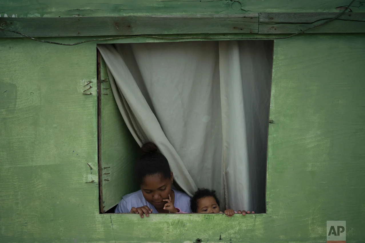 In this June 6, 2017 photo, Suzi Souza dos Santos and her baby Maria Lais stand in the window of their small wooden home in one of the poorest areas of the City of God slum in Rio de Janeiro, Brazil. (AP Photo/Leo Correa)