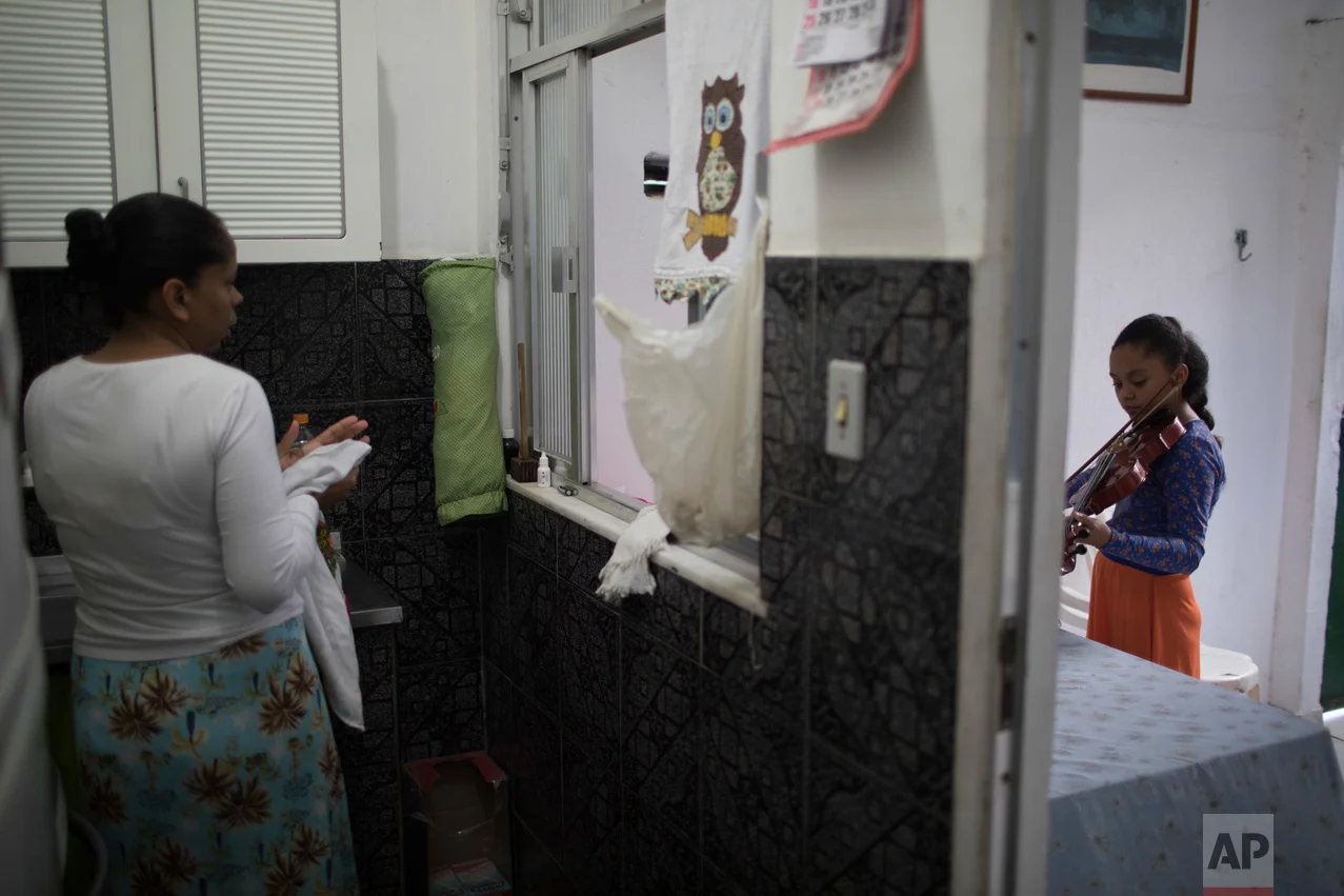 In this June 9, 2017 photo, Isabela Maia practices the violin as her mother works in the kitchen at their home in the City of God slum of Rio de Janeiro, Brazil. (AP Photo/Leo Correa)