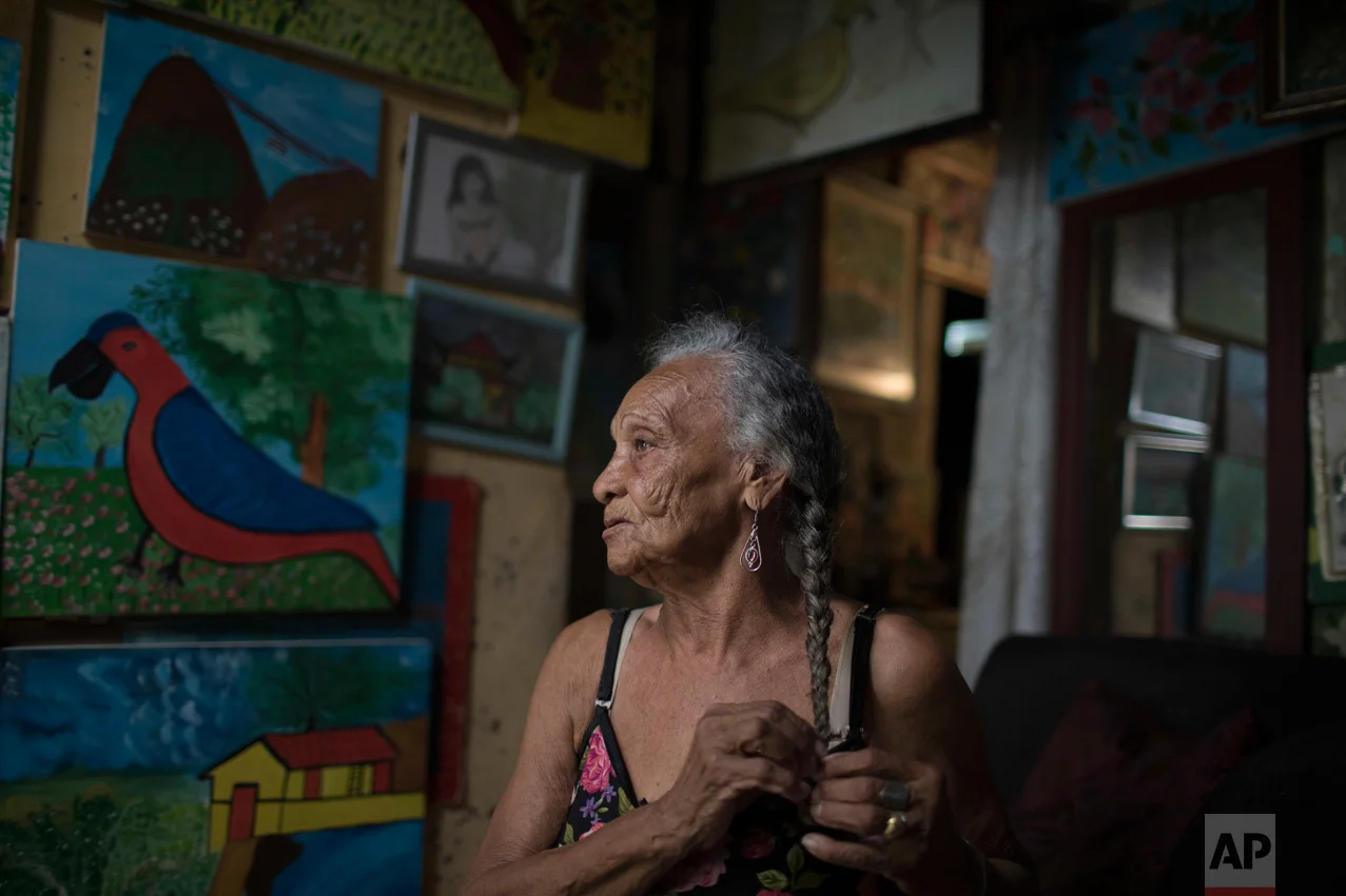 In this June 9, 2017 photo, artist Anayde dos Santos Muniz, affectionately known as "Tuca," poses for a portrait surrounded by her paintings inside her home in the City of God slum of Rio de Janeiro, Brazil. (AP Photo/Leo Correa)