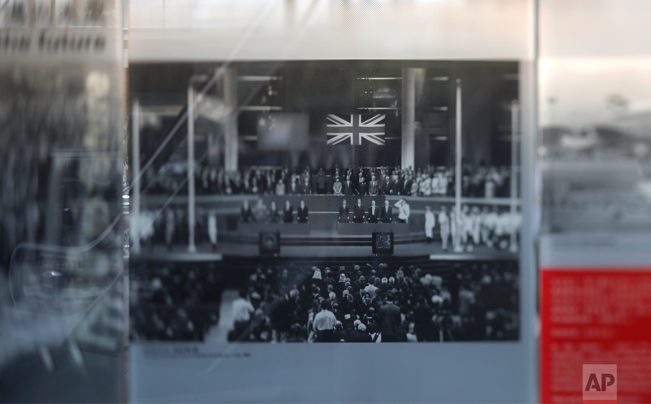 In this June 27, 2017, photo made with a tilt-shift lens, a photograph showing Chinese and British flags during the ceremony for the handover of Hong Kong to China on July 1, 1997, is displayed at an exhibition in Hong Kong. Two decades since Beijing took control of Hong Kong, China's rising influence – and Britain's waning profile – are impossible to ignore. (AP Photo/Vincent Yu)