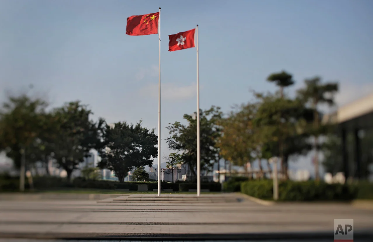 In this May 29, 2017, photo made with a tilt-shift lens, a Chinese national flag and a Hong Kong flag are flown at the Legislative Council, the legislature of Hong Kong. In Hong Kong's semi-democratic 70-seat Legislative Council, some lawmakers are directly elected and others represent business and professional groups, in a system that pro-democracy supporters complain lets Beijing maintain a disproportionate level of control. Two decades since Beijing took control of Hong Kong, China's rising influence – and Britain's waning profile – are impossible to ignore. (AP Photo/Vincent Yu)