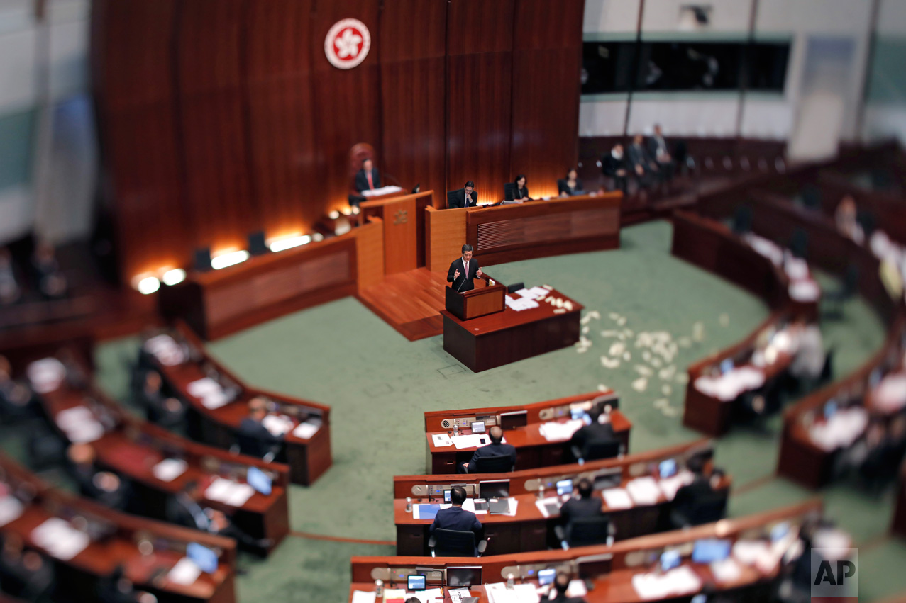 In this June 1, 2017, photo made with a tilt-shift lens, Hong Kong Chief Executive Leung Chun-ying, center, speaks after lawmaker Leung Kwok-hung, also known as Long Hair threw "hell money" during his last question-and-answer session at the legislative council in Hong Kong. Hong Kong's departing leader, Leung Chun-ying, also known as CY, is viewed by pro-democracy activists as a puppet of Beijing. Two decades since Beijing took control of Hong Kong, China's rising influence – and Britain's waning profile – are impossible to ignore. (AP Photo/Vincent Yu)