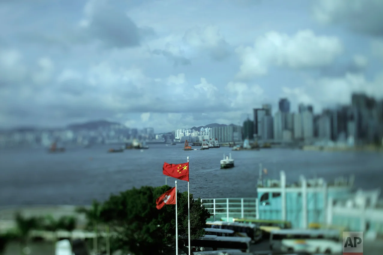In this June 8, 2017, photo made with a tilt-shift lens, a Chinese national flag and a Hong Kong flag are flown as Victoria Harbor is seen at rear in Hong Kong. Hong Kong's famous waterfront retains its British colonial-era name and was the scene of Britain's farewell from its colony in 1997. Two decades since Beijing took control of Hong Kong, China's rising influence – and Britain's waning profile – are impossible to ignore. (AP Photo/Vincent Yu)