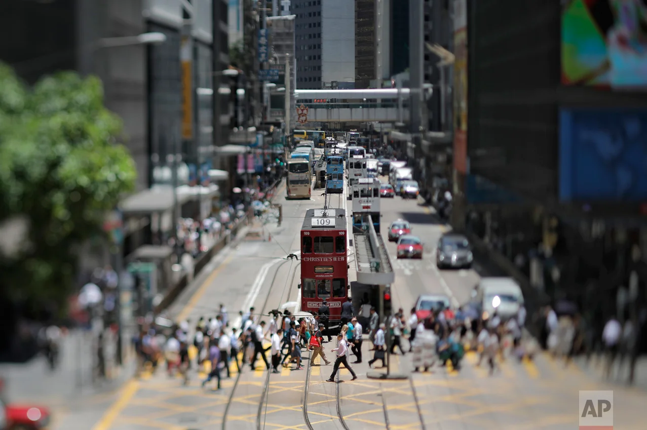 In this May 31, 2017, photo made with a tilt-shift lens, people walk at Central district in Hong Kong. Two decades since Beijing took control of Hong Kong, China's rising influence – and Britain's waning profile – are impossible to ignore. (AP Photo/Vincent Yu)