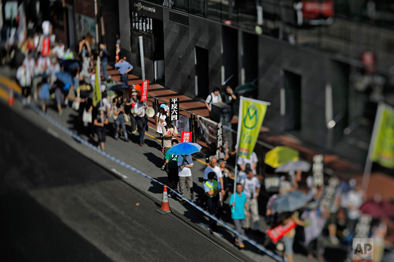 In this May 28, 2017, photo made with a tilt-shift lens, protesters in Hong Kong carry placards with Chinese words that read: "Exonerate the June 4 Protest" as hundreds of Hong Kong people march on a downtown street to mark the 28th anniversary of China's crackdown on Tiananmen Square. Two decades since Beijing took control of Hong Kong, China's rising influence – and Britain's waning profile – are impossible to ignore. (AP Photo/Vincent Yu)