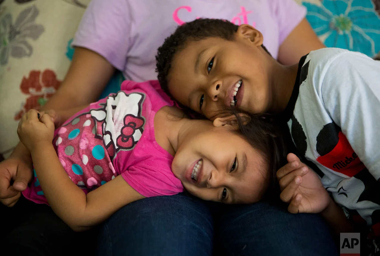 In this June 22, 2017 photo, Carlita Perez, 3, from El Salvador, and Josue Funez Cruz, 7, from Honduras, play together on the lap of Josue's sister Laura, 14, in the two-bedroom apartment the families share in the Iztapalapa district of Mexico City. (AP Photo/Rebecca Blackwell)