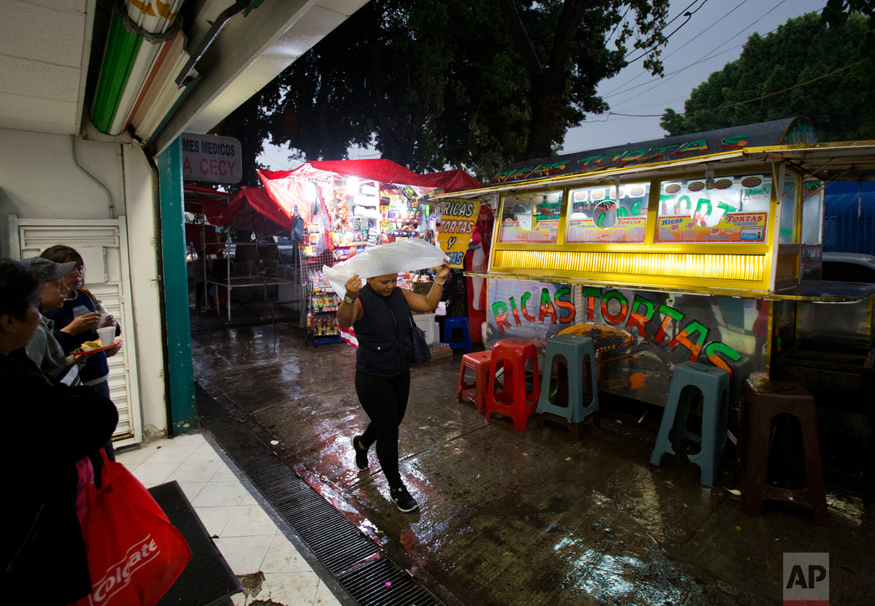 In this June 27, 2017 photo, Honduran refugee Laura Maria Cruz Martinez shields herself from a rainy season downpour with a thin plastic poncho as she walks from the medical supply store where she works to the nearest subway station, in the Doctores neighborhood of Mexico City. (AP Photo/Rebecca Blackwell)