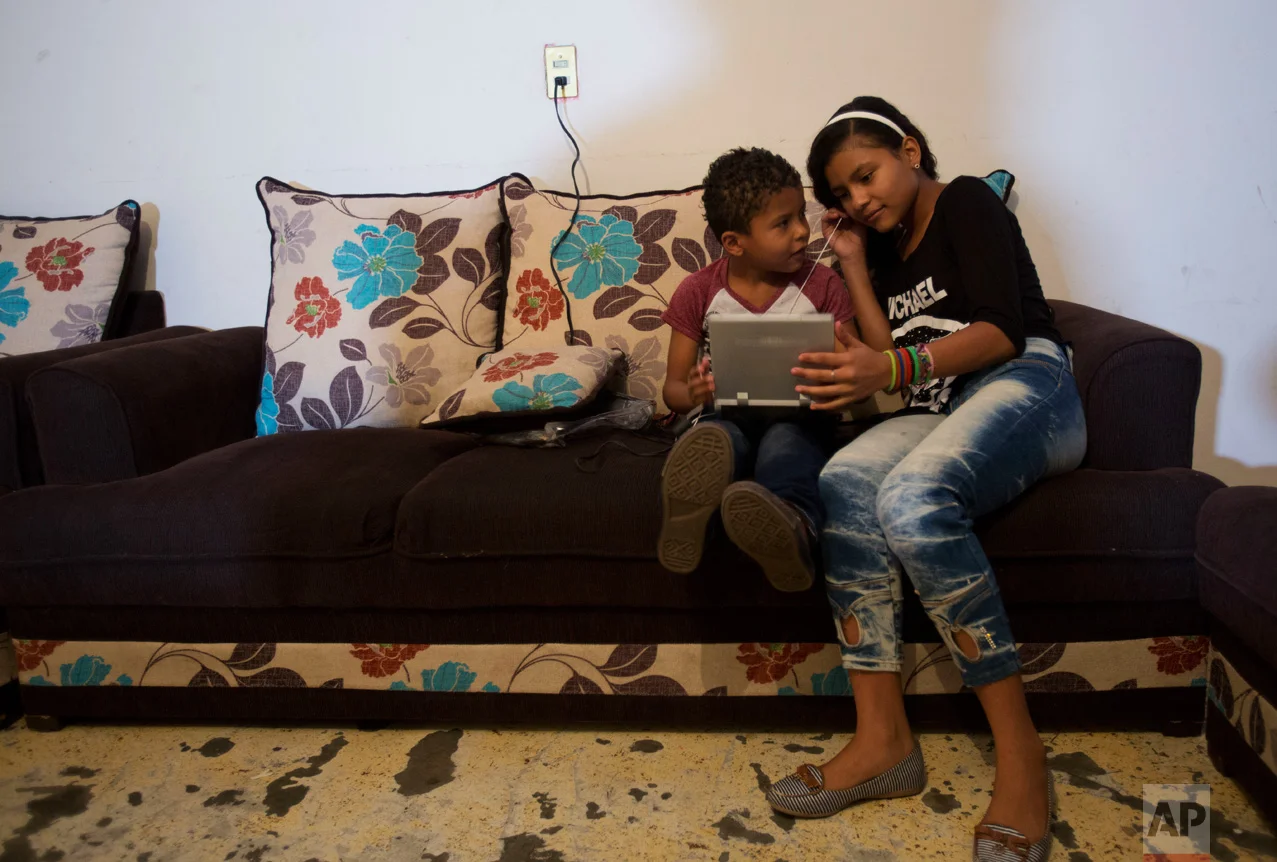 In this June 27, 2017 photo, Ruth Funez Cruz, 12, and her brother Josue, 7, try to watch a pirated DVD on a portable player with broken headphones, in the two-bedroom apartment they share with another refugee family in Mexico City. (AP Photo/Rebecca Blackwell)