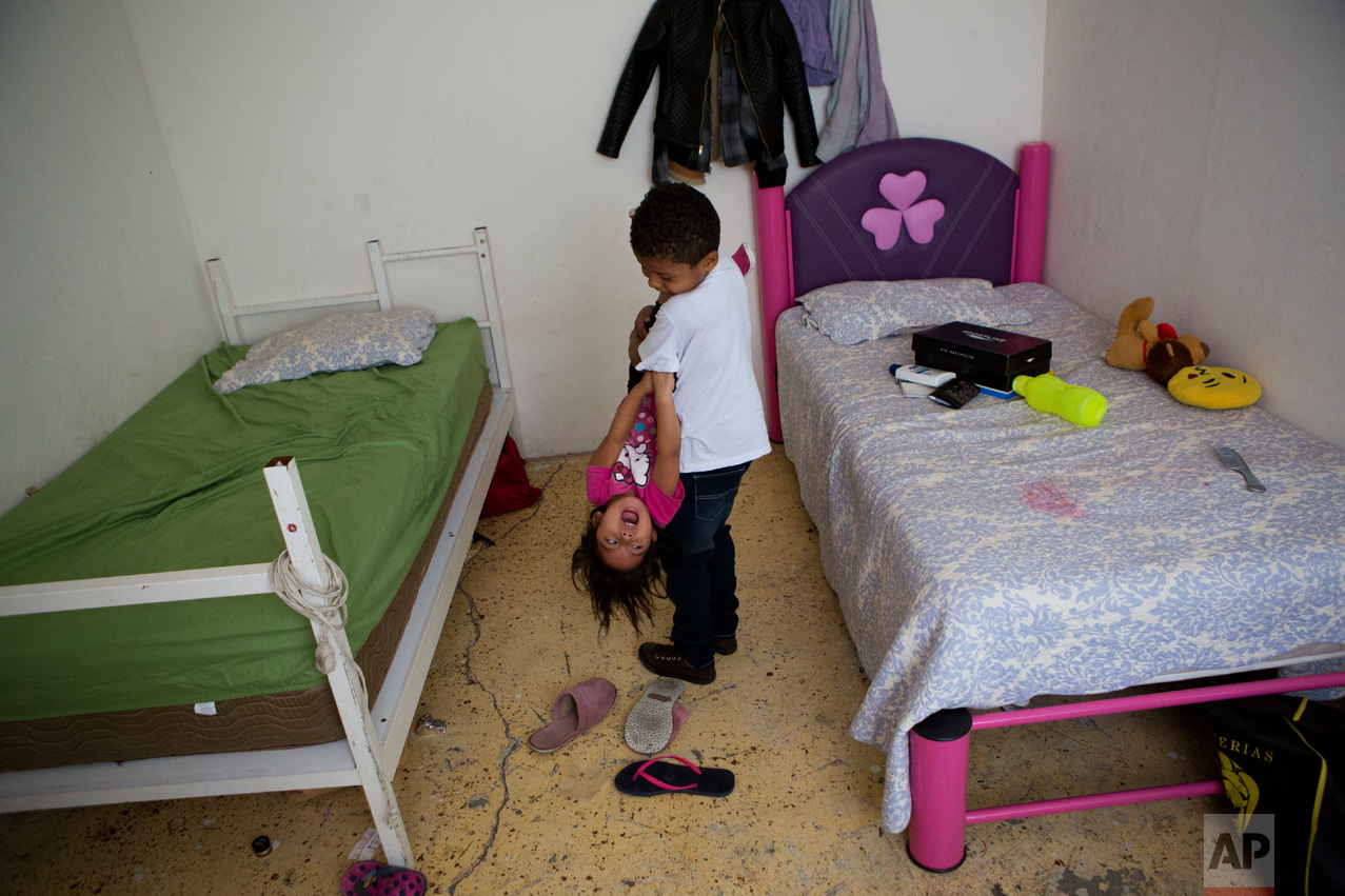In this June 22, 2017 photo, Josue Funez Cruz, 7, from Honduras, carries Carlita Perez, 3, from El Salvador, as they play together in the two-bedroom apartment their families share in the Iztapalapa district of Mexico City. (AP Photo/Rebecca Blackwell)