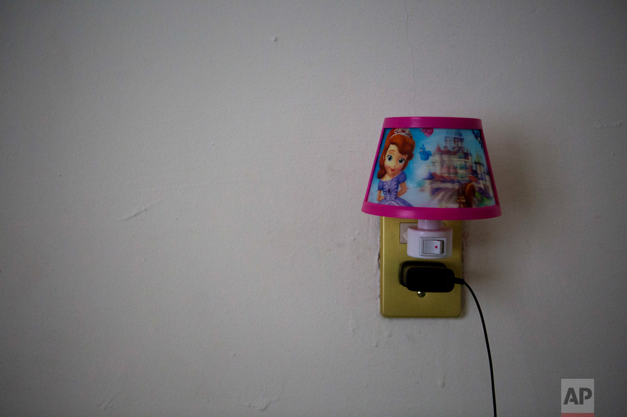 In this June 22, 2017 photo, a nightlight with images from Disney's "Frozen," is plugged into a socket in the bedroom of Carlita Perez, 3, from El Salvador, and her mother in the two-bedroom apartment they share with Laura Maria Cruz Martinez of Honduras and her family, in the Iztapalapa district of Mexico City. (AP Photo/Rebecca Blackwell)