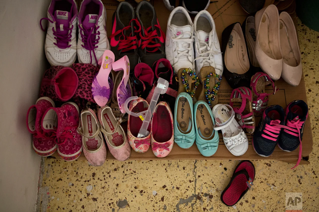 In this June 22, 2017 photo, donated shoes are laid out on cardboard in the bedroom of El Salvadoran refugees Carlita Perez, 3, and her mother in the two-bedroom apartment they share with Laura Maria Cruz Martinez of Honduras and her family, in the Iztapalapa district of Mexico City. (AP Photo/Rebecca Blackwell)