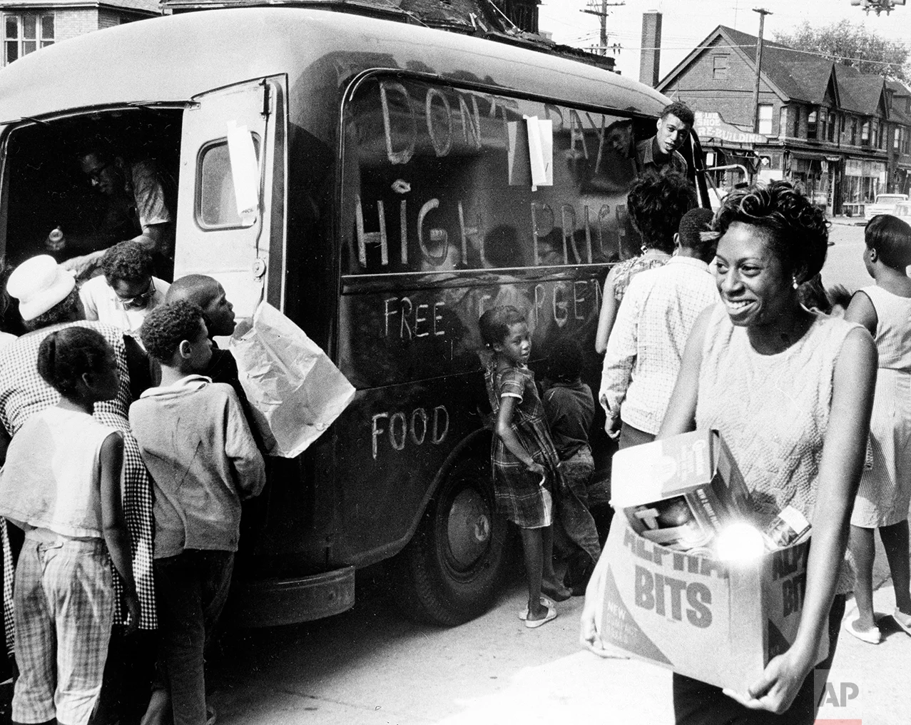 People gather around a truck to get free food on Detroit's east side, July 27, 1967. The food was brought to the riot-stricken area by the Crisis Council, one of the many organizations aiding residents. Sign on the side of the truck reads "Don't pay high prices - free emergency food." (AP Photo)