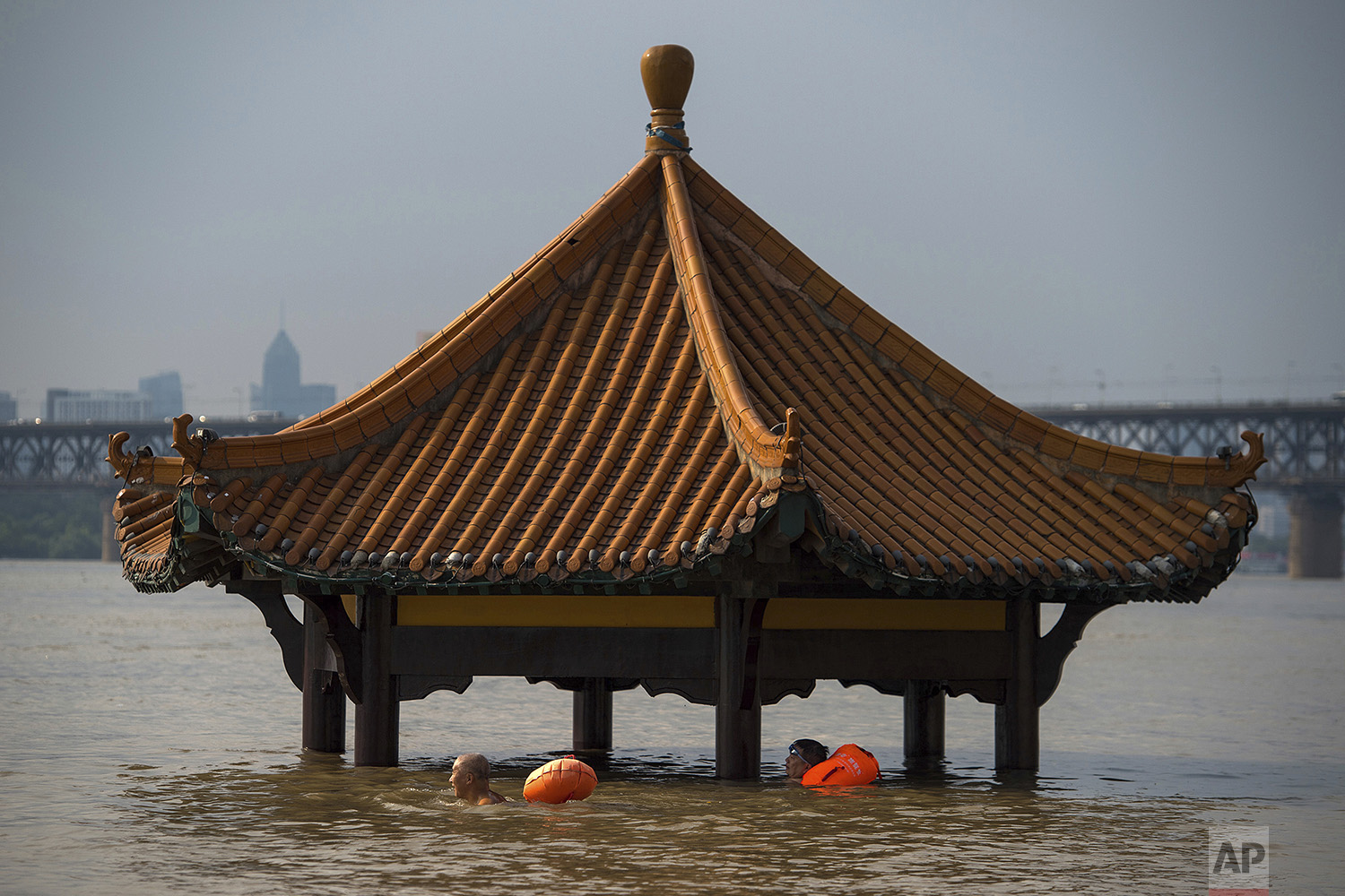 People swim past the top of a pagoda at a flooded riverside park in Wuhan in central China's Hubei Province on Monday, July 3, 2017. (Chinatopix via AP)