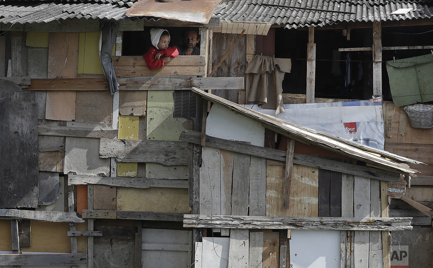 A boy peers from his home's window as firefighters extinguish the last flames of a nearby fire in the Osasco neighborhood of the greater Sao Paulo area of Brazil, Monday, July 3, 2017. (AP Photo/Andre Penner)