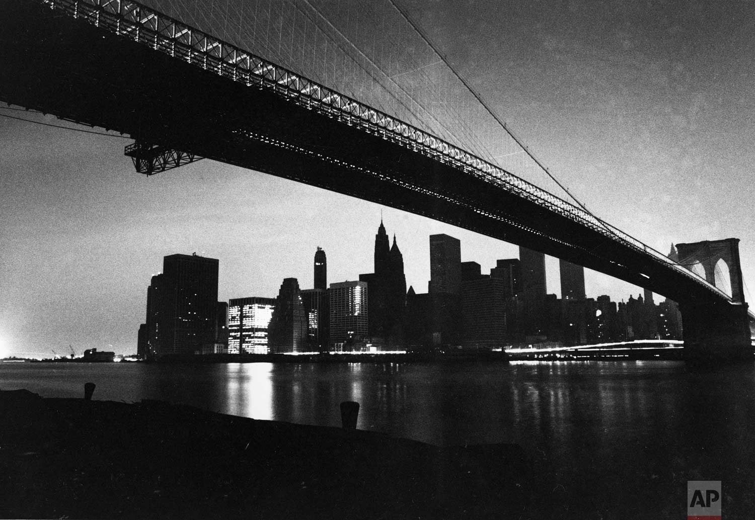  The lights of lower Manhattan are dark as a result of an electrical power failure in this view from under the Brooklyn Bridge on Wednesday, July 13, 1977.  One building at left is lit with emergency power and a stream of light comes from the headlig