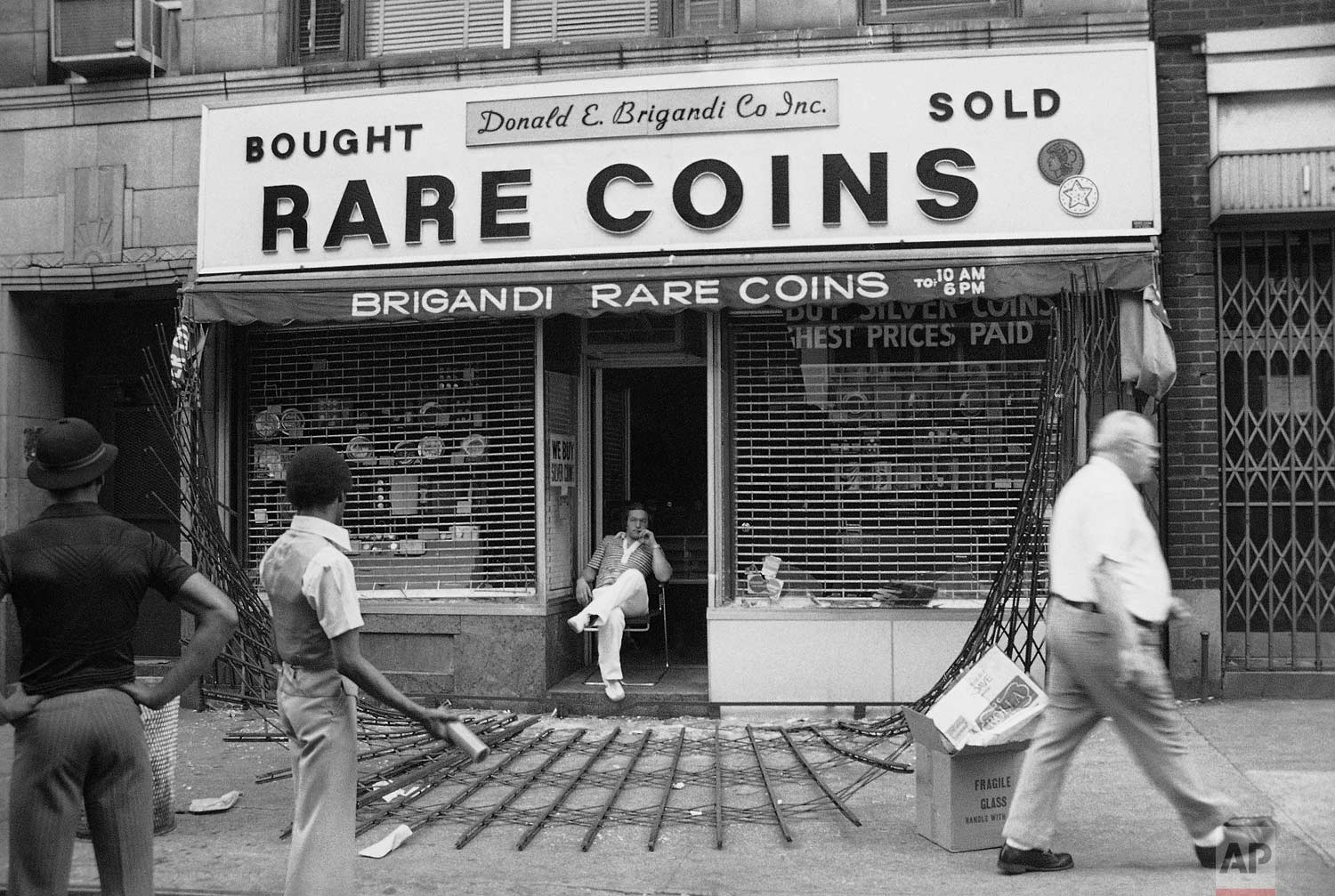  The owner of midtown Manhattan coin shop sits disconsolately in his doorway in New York on Thursday, July 14, 1977. The steel gates protecting the shop were ripped down by looters. "They sure cleaned me out," he said. (AP Photo/Sandy Colton) 