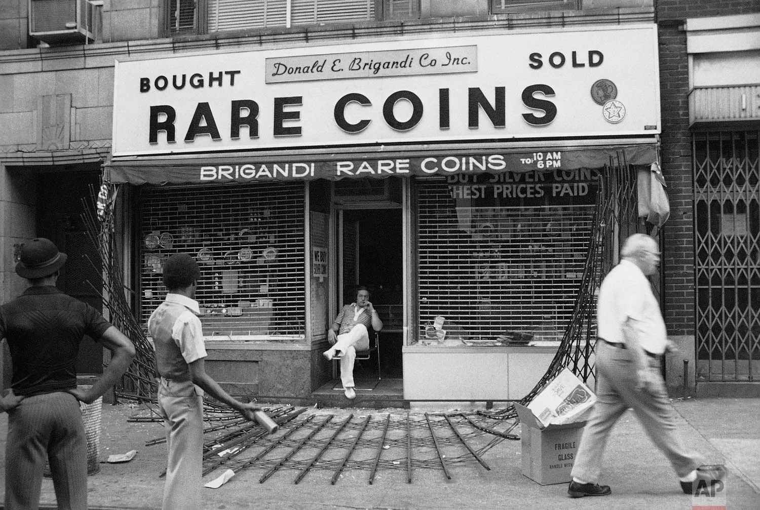 The owner of midtown Manhattan coin shop sits disconsolately in his doorway in New York on Thursday, July 14, 1977. The steel gates protecting the shop were ripped down by looters. "They sure cleaned me out," he said. (AP Photo/Sandy Colton)
