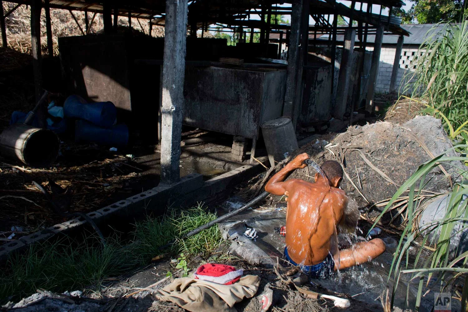 In this June 19, 2017 photo, a man washes off at the end of his eight-hour shift carrying bagasse, the fiber left over after pressing juice from sugar cane, at the Ti Jean distillery, which produces clairin, a sugar-based alcoholic drink, in Leogane, Haiti. Clairin, or kleren as it's known in Haitian Creole, is produced at hundreds of small distilleries scattered throughout Haiti. (AP Photo/Dieu Nalio Chery)