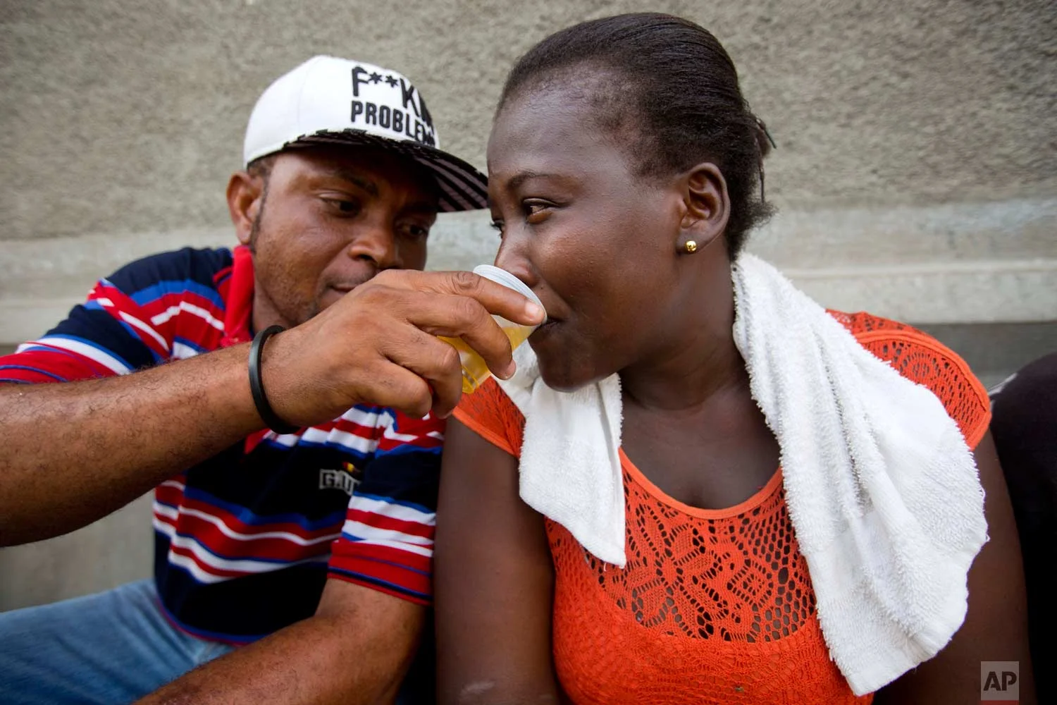 A man shares his clairin as he sits on the sidewalk where a vendor sells the sugar-based alcoholic drink in the Cite Soleil area of Port-au-Prince, Haiti, Tuesday, July 11, 2017. Clairin is rum's rustic cousin, a drink that's much cheaper and relatively rare outside this struggling Caribbean country. (AP Photo/Dieu Nalio Chery)