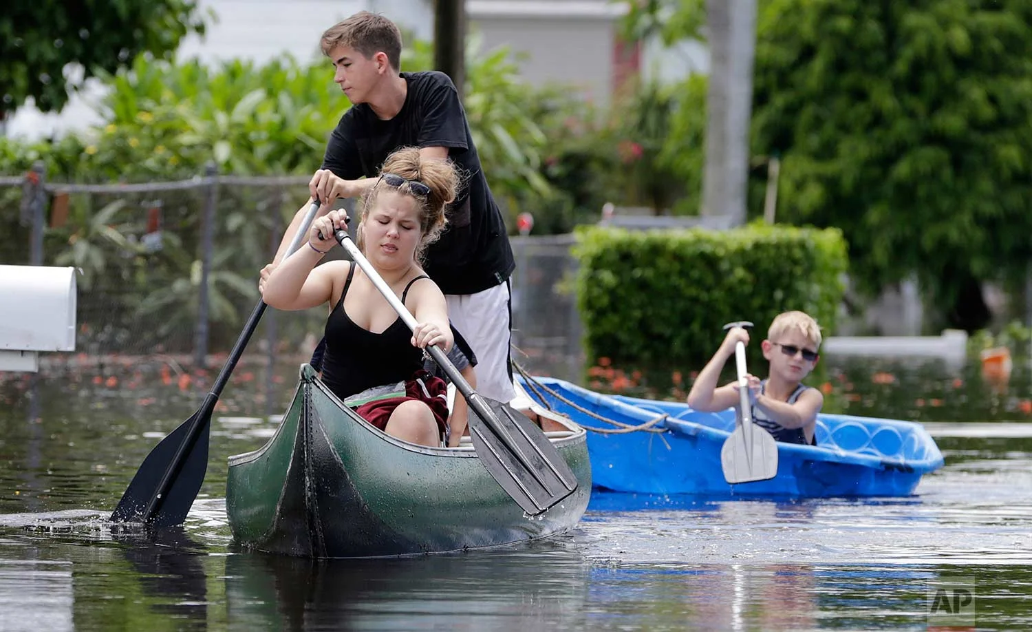 Isabella and Timothy, who did not want their last names used, navigate flooded streets following heavy rains, Wednesday, June 7, 2017, in Davie, Fla. Several South Florida cities set rainfall records as heavy rain continues to fall, bringing the potential for further flooding. Wallace put up the "Slow No Wake" sign to prevent fast moving vehicles from flooding her trailer. (AP Photo/Lynne Sladky)