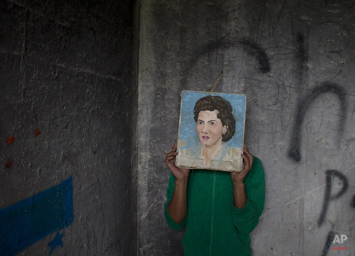  In this Wednesday, July 30, 2014 photo, a young Honduran migrant who didn't want his face to appear in photos hides behind a painting he found in a guard shack, while waiting with a group of migrants for a northbound train, in Huehuetoca, outside Me