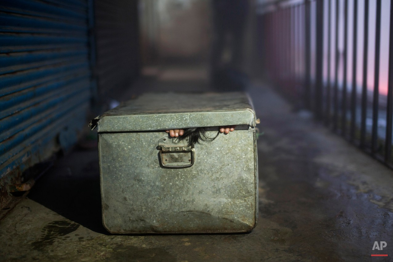  In this Sunday, Sept. 28, 2014 photo, a young Tibetan exile Pema Lhamo, 8, fits herself into a box to enact her escape scene, in Dharmsala, India. Lhamo fled to India when she was 3 years old in a box and now lives with her grandmother. She is prese
