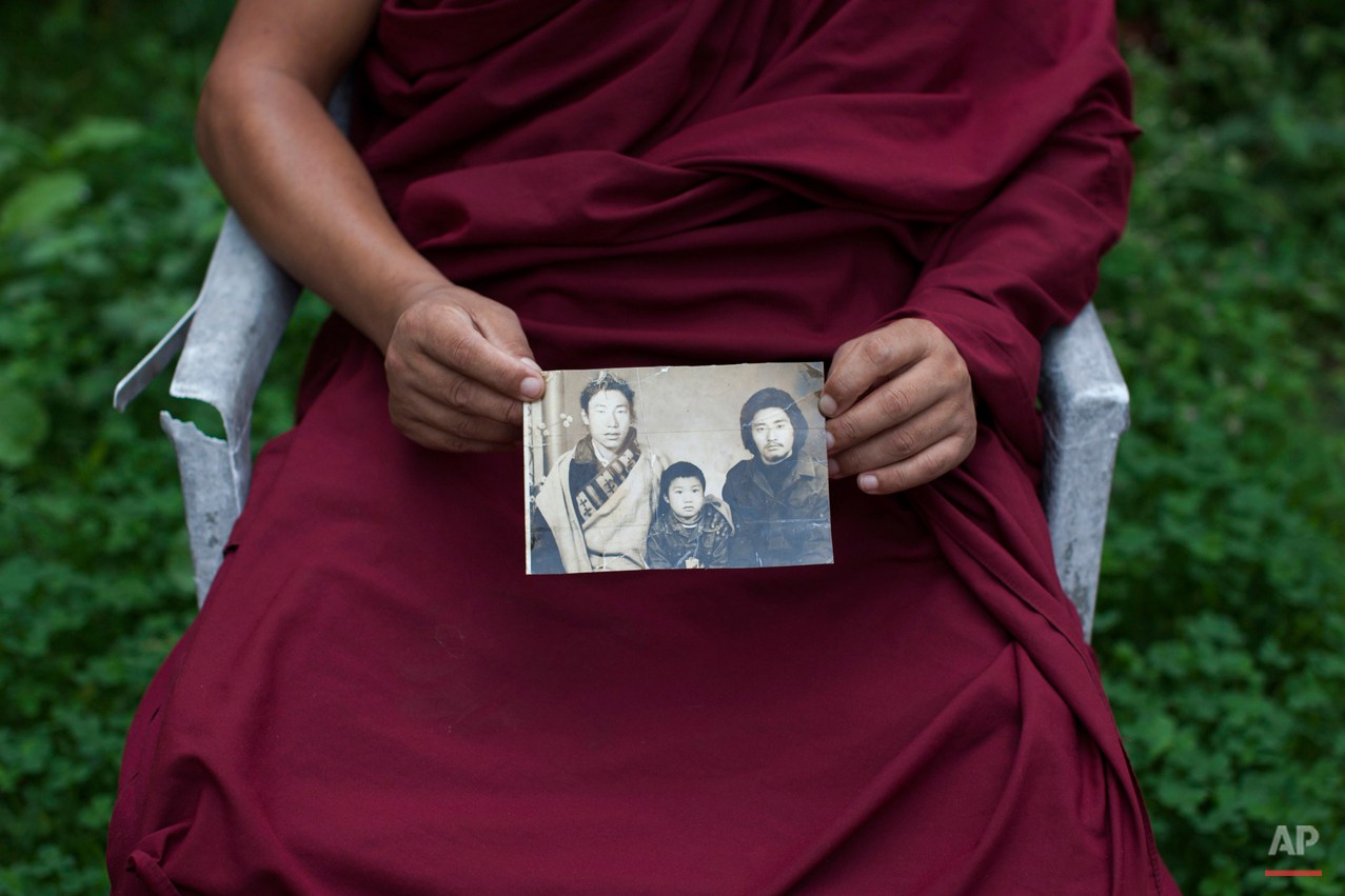  In this Saturday, Sept. 27, 2014 photo, Tibetan monk Dorjee, 38, displays a photograph of his father, left, and himself, center, taken in Tibet, in Dharamsala, India. Dorjee said he held back his tears when he spoke with his parents on the phone aft