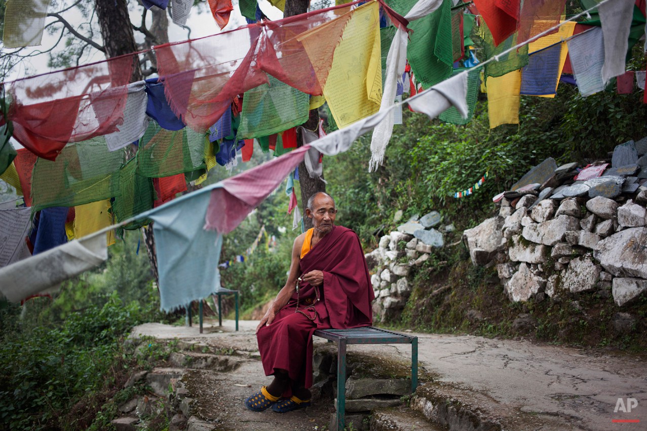  In this Thursday, Sept. 25, 2014 photo, Tibetan exile monk Lobsang Tenzin, 76, sits near prayer flags in Dharmsala, India. Tenzin lives in a home for the aged supported by the Tibetan government-in-exile. He fled Tibet in 2006 leaving his entire fam