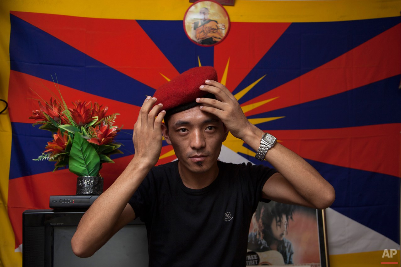  In this Friday, June 6, 2014 photo, Exile Tibetan Dorjee Tashi adjust the beret he calls "Che Guevera cap" as he poses for a photograph in front of a flag of Tibet in his room in New Delhi, India. Tashi had just returned from a protest rally when he