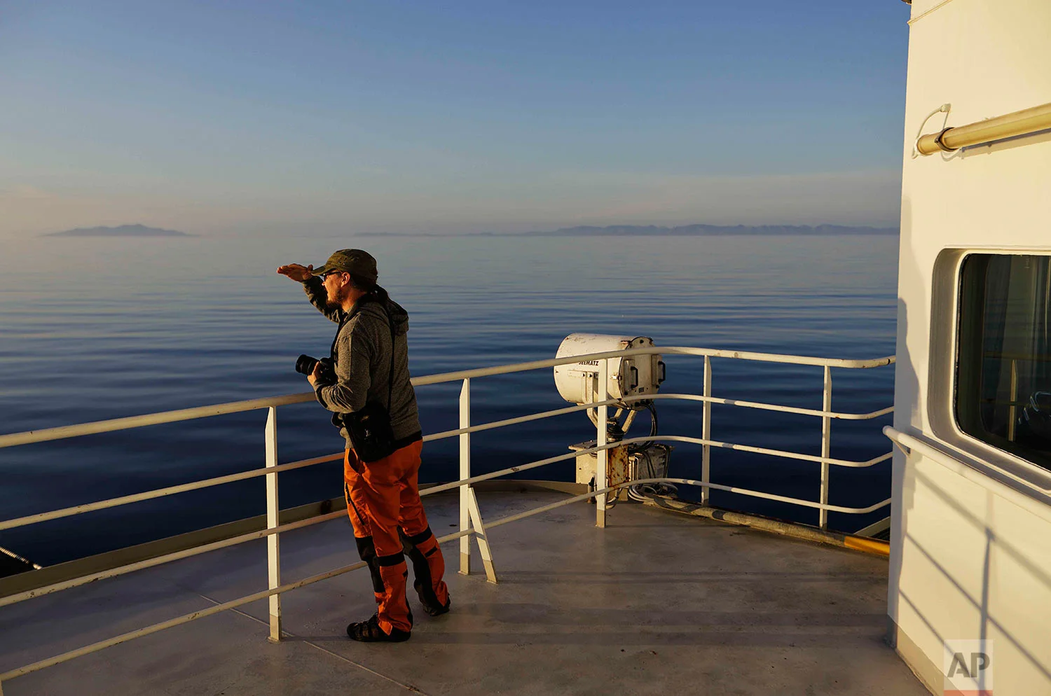 Researcher Ari Laakso shields his eyes from the midnight sun while approaching the American island of Little Diomede, Alaska, and the Russian island of Big Diomede, as the Finnish icebreaker MSV Nordica sails along the international date line through the Bering Strait, Friday, July 14, 2017. The international date line divides the two islands, putting them currently 20 hours apart despite roughly 2.4 miles (3.8 kilometers) between them. (AP Photo/David Goldman)
