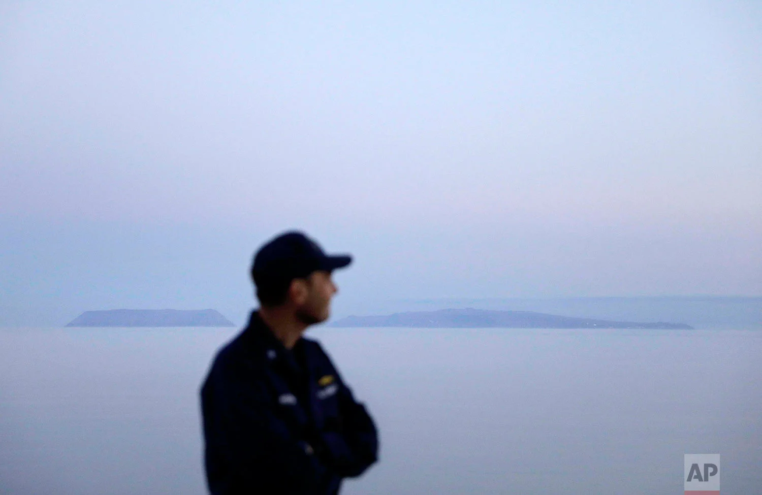 Cmdr. Bill Woityra, manager for domestic and polar icebreaking for the U.S. Coast Guard, looks out to sea while passing the American island of Little Diomede, Alaska, left, and the Russian island of Big Diomede, right, as the Finnish icebreaker MSV Nordica sails along the international date line through the Bering Strait, Friday, July 14, 2017. The international date line divides the two islands, so Little Diomede is sometimes referred to as Yesterday Isle and Big Diomede as Tomorrow Island. (AP Photo/David Goldman)