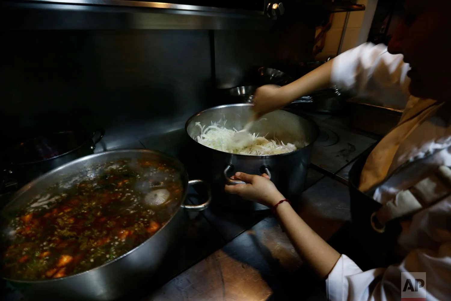 In this July 13, 2017 photo, a kitchen staff worker cooks onions and beans with "epazote" herbs at the Maximo Bistrot restaurant in Mexico City. (AP Photo/Marco Ugarte)