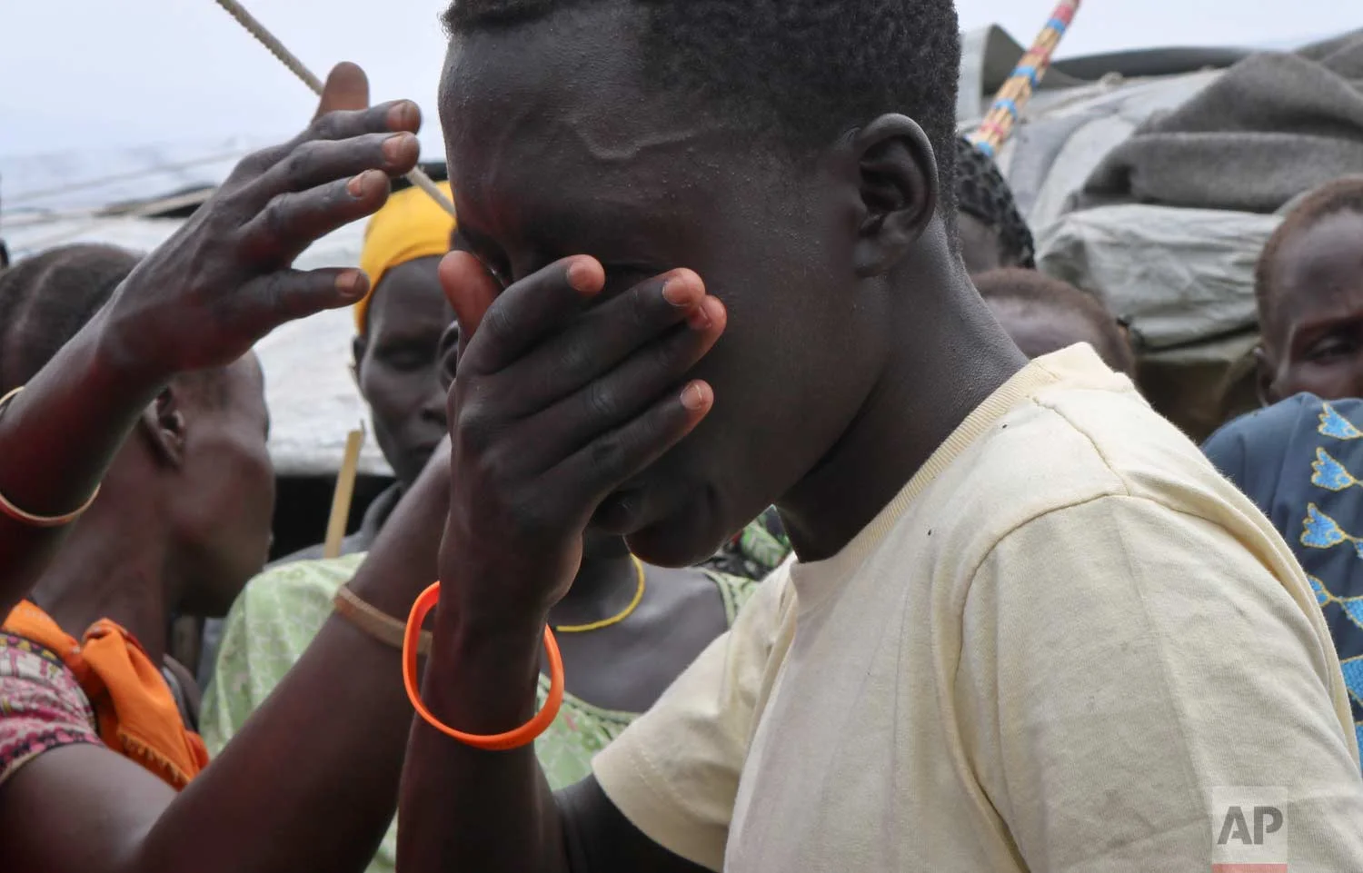 In this photo taken Friday, May 26, 2017, former child soldier James cries uncontrollably as he is reunited with his mother for the first time in 3 years, while family and friends brush their hands over his face in a Nuer tradition that wishes him a long life, at a protection of civilians site in Bentiu, South Sudan. (AP Photo/Sam Mednick)